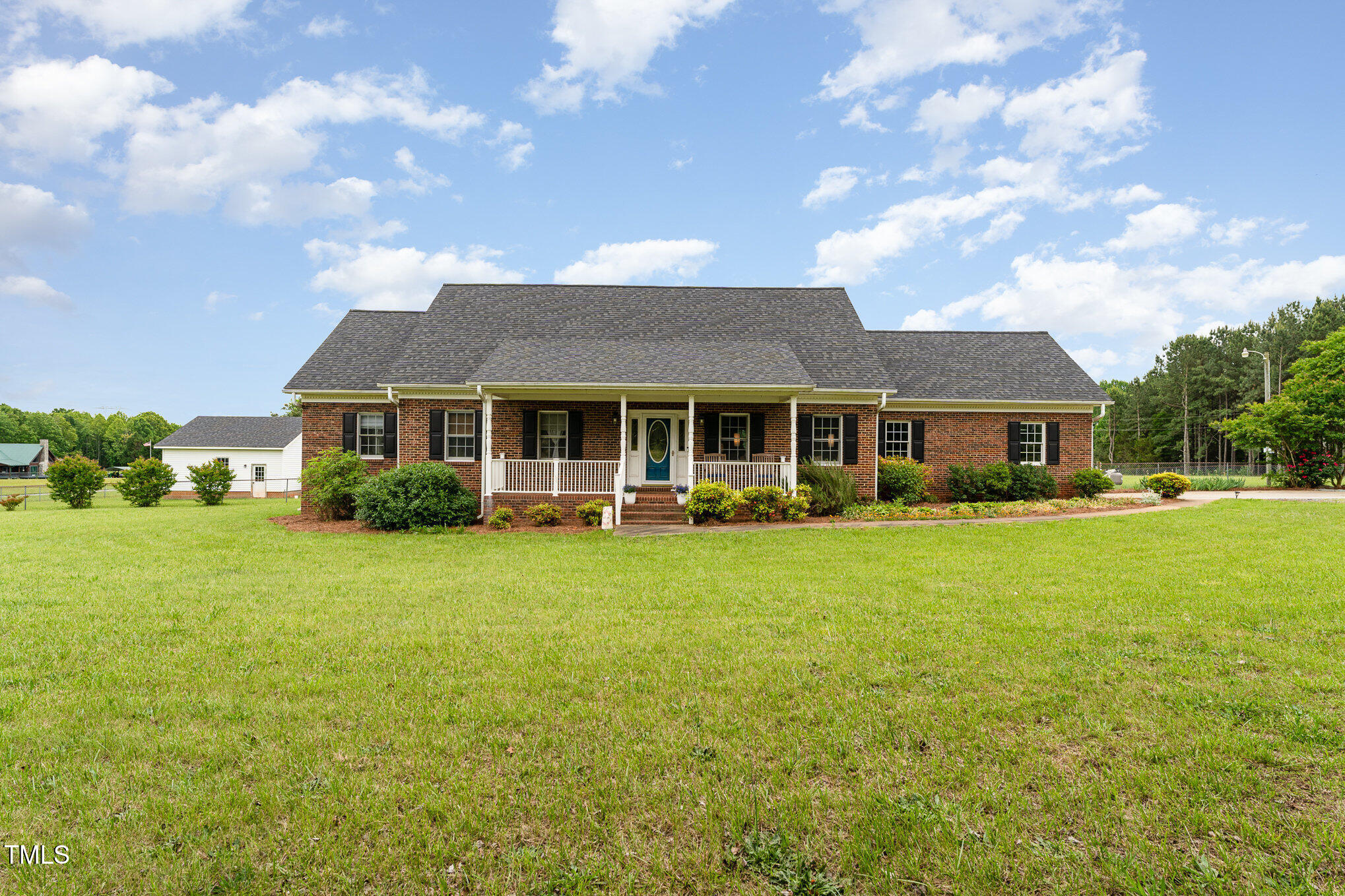 Single-story brick house with a covered porch, teal front door, and broad green lawn.
