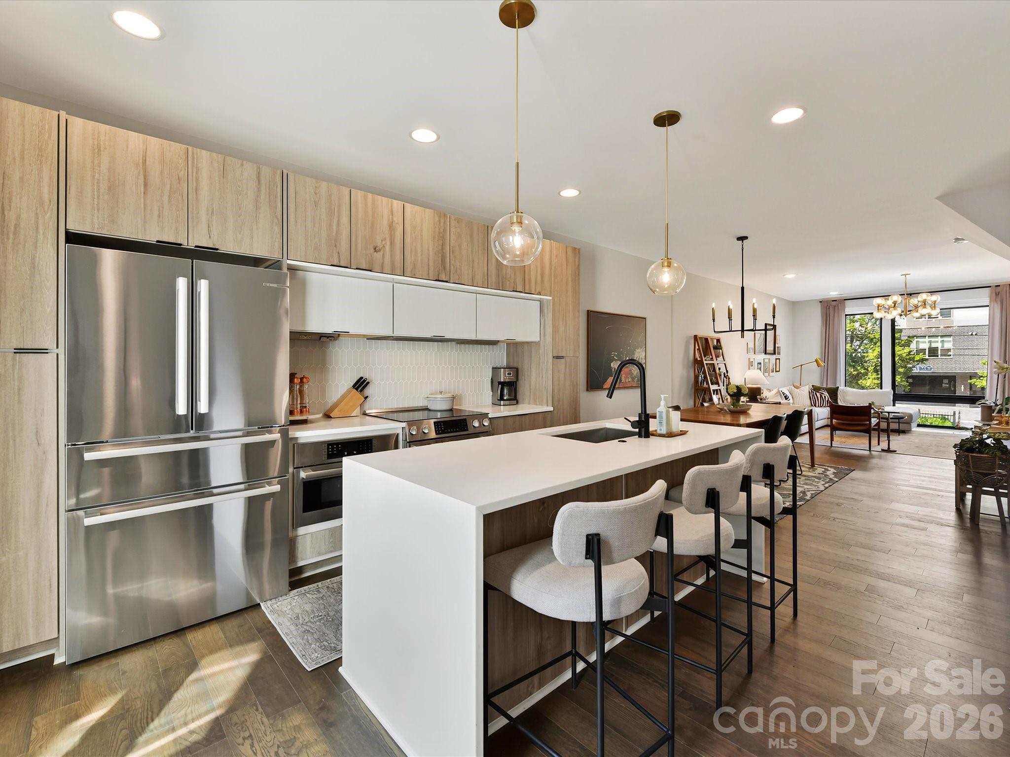 Open-plan condo kitchen with light wood cabinets, stainless appliances, and a large island with bar seating.