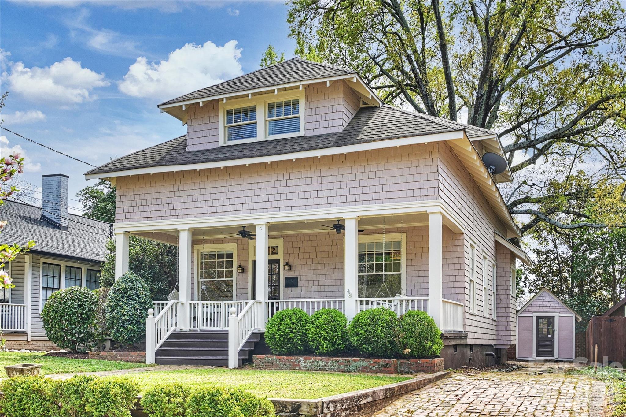 Shingle-sided house with a covered porch, upper dormer, and small matching outbuilding.