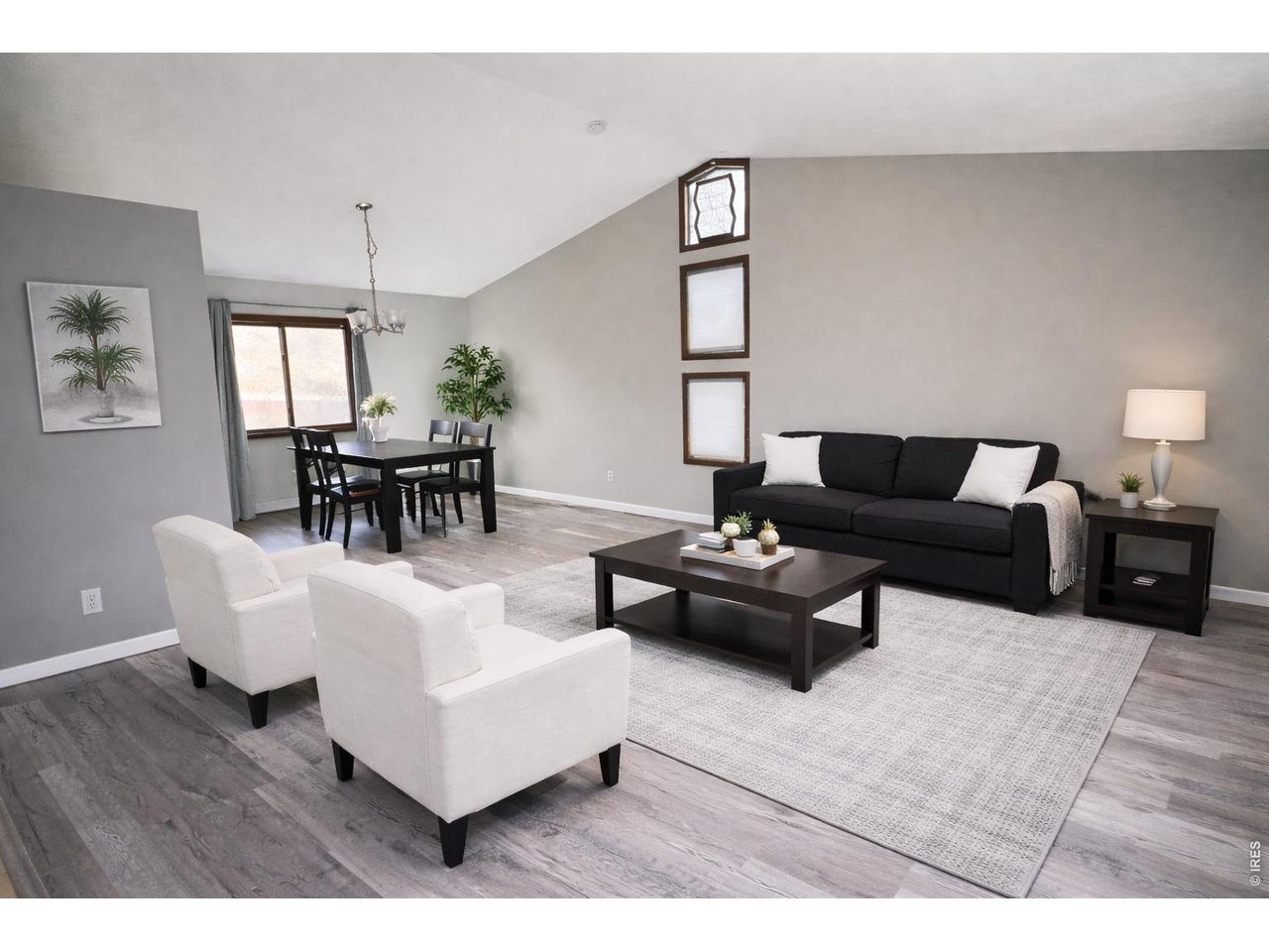 Staged living room with black sofa, white armchairs, and an adjoining dining area.
