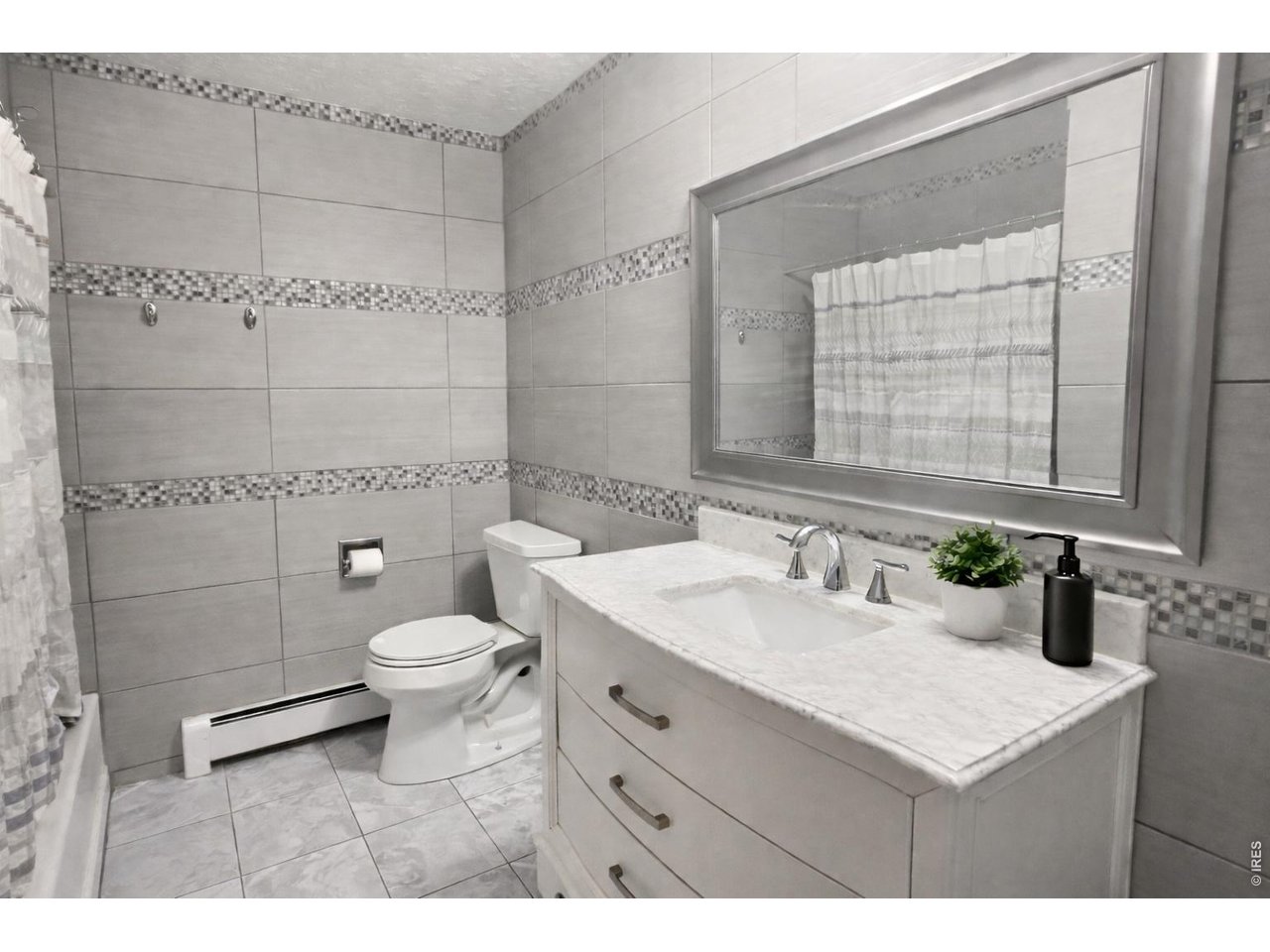 Bathroom with gray tiled walls, mosaic accents, and a white vanity with a marble-look counter.