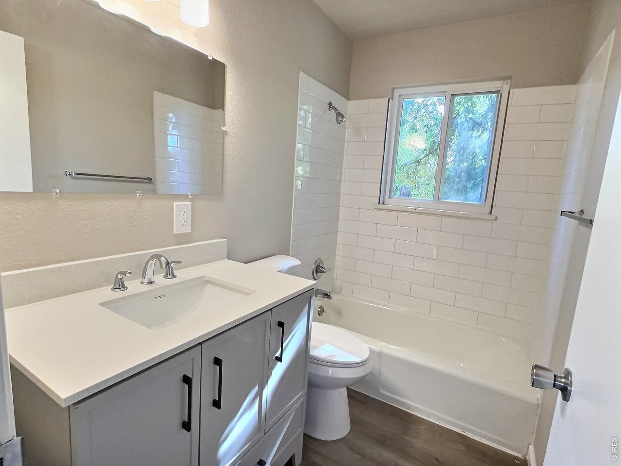 Bathroom with a gray vanity, white subway-tiled tub surround, and window above the bathtub.