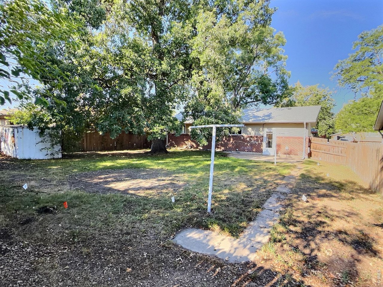 Brick home's fenced backyard with a large shade tree, white shed, and concrete path.