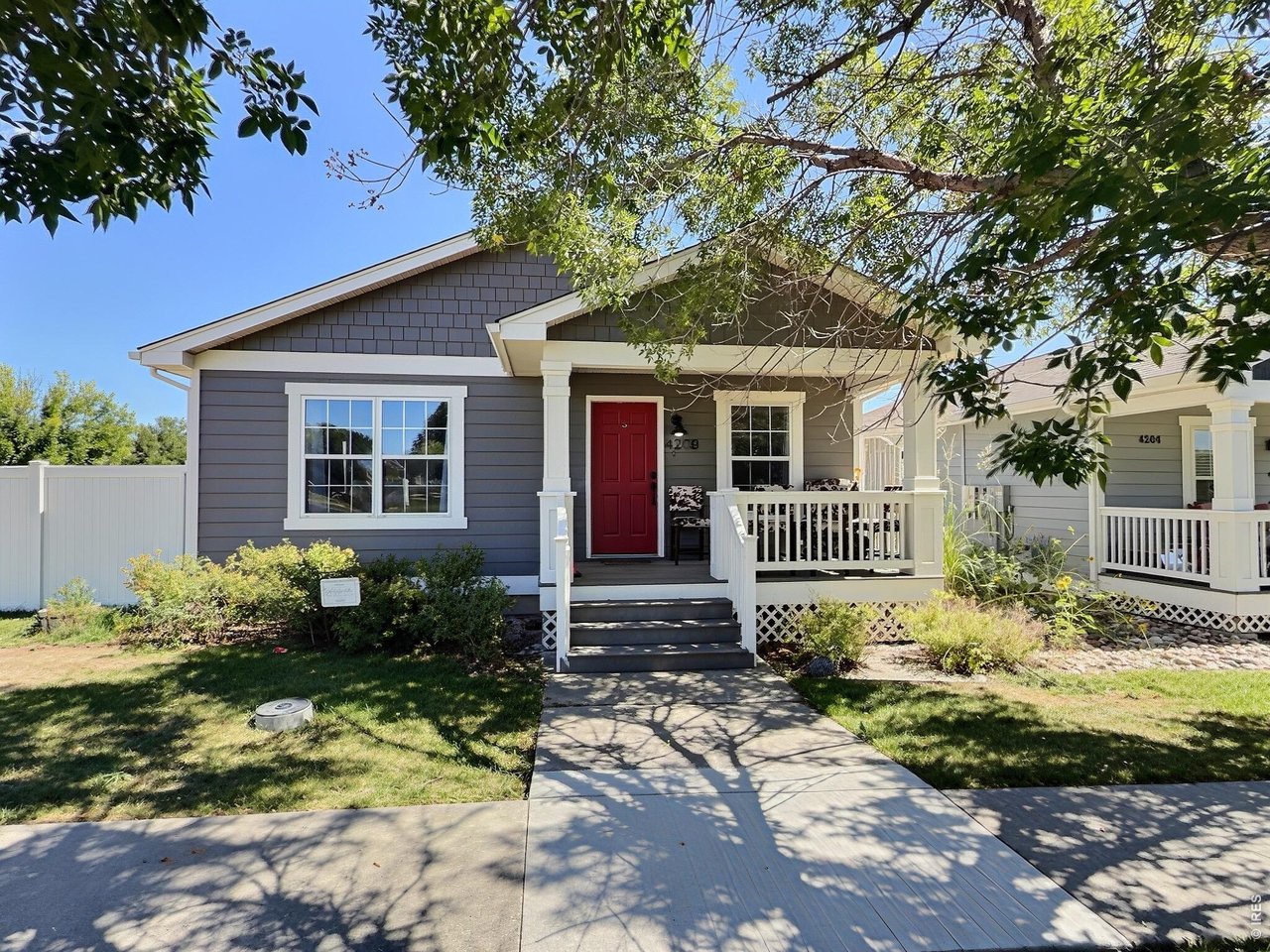 Gray home with white trim, red front door, covered porch, and leafy trees.