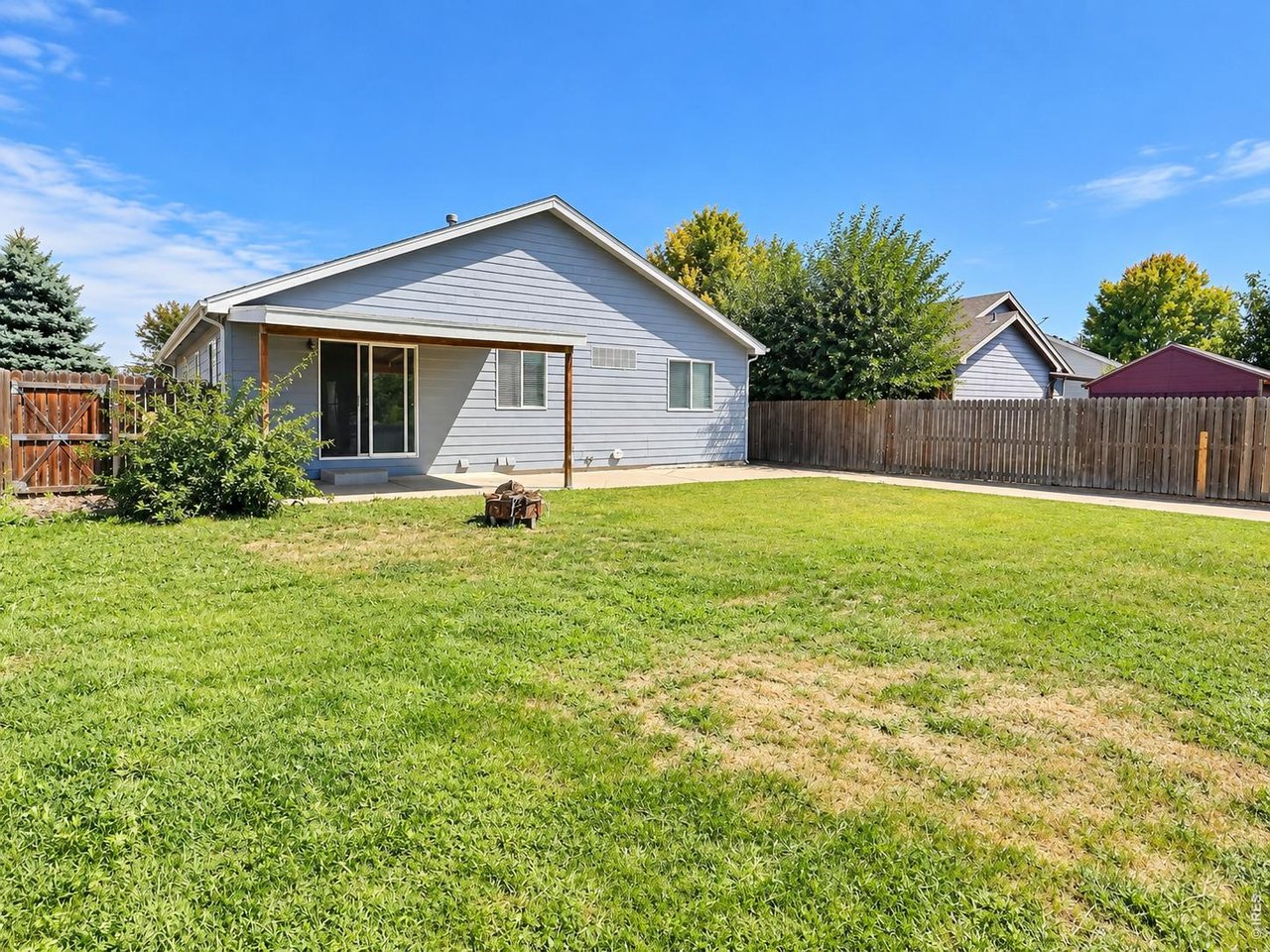 Gray-sided home with a covered patio and sliding door overlooking a fenced backyard and broad lawn.