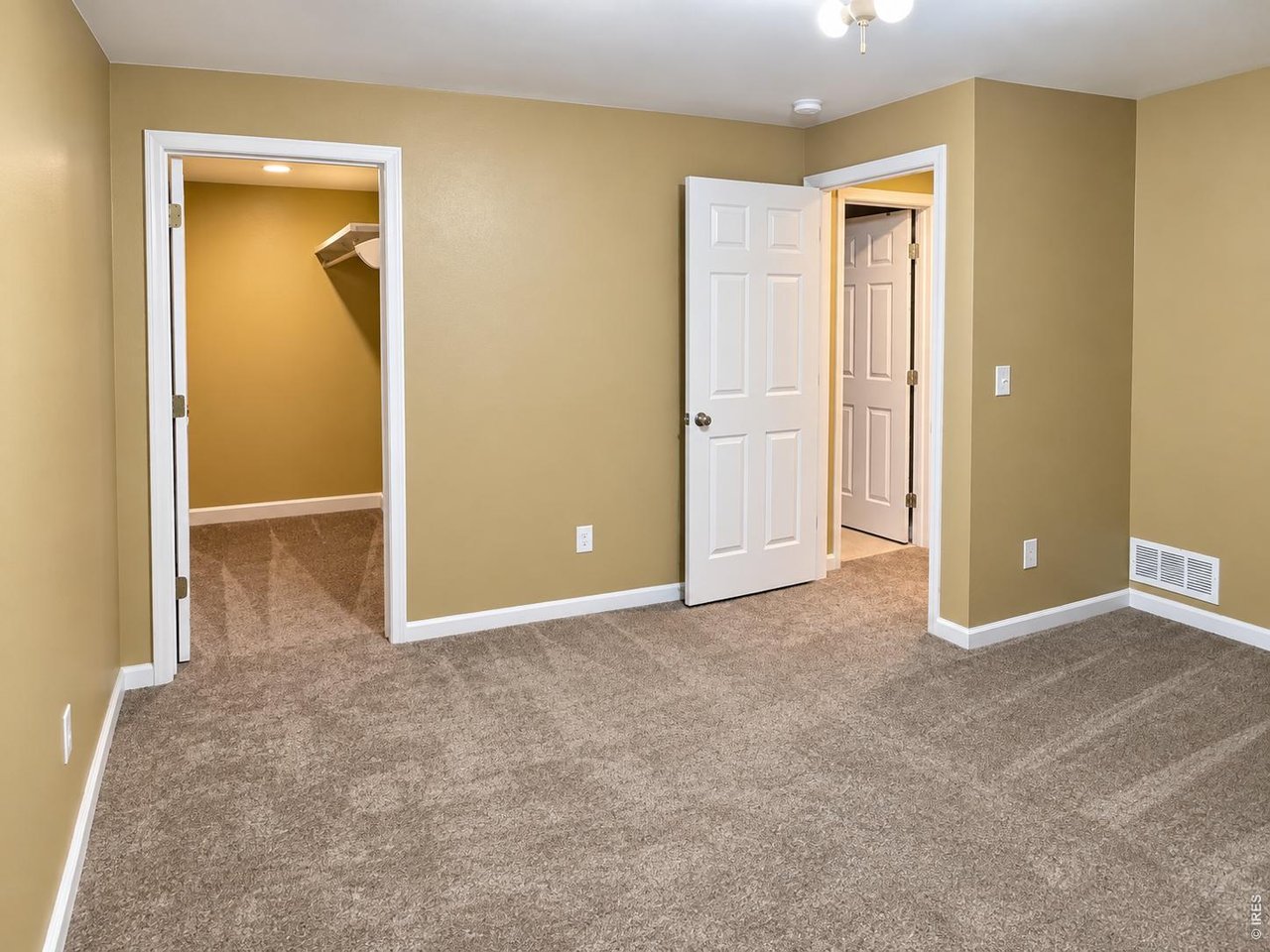 Empty carpeted room with tan walls, an open closet, and doors leading to the hall.