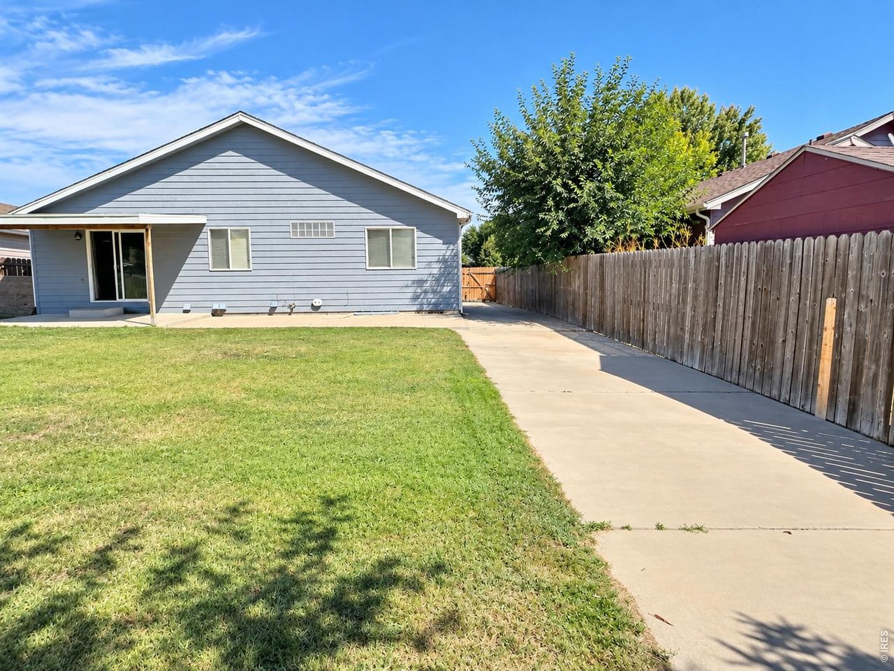 Rear of a blue-gray home beside a lawn, concrete walkway, and wooden privacy fence.