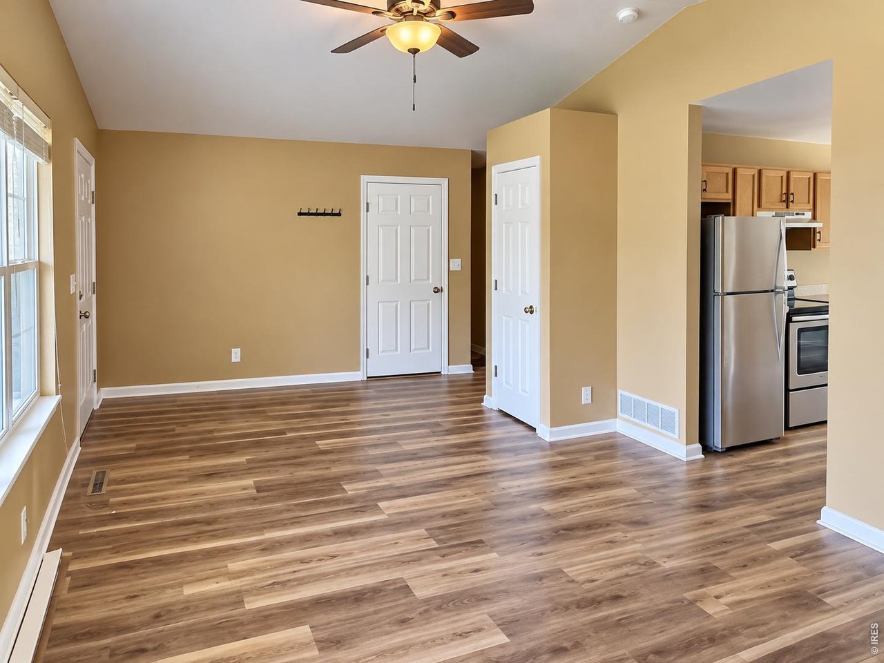Empty room with wood-look flooring and a ceiling fan, opening to a kitchen.