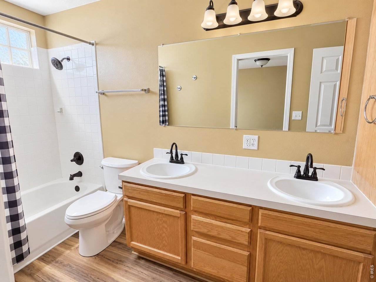 Bathroom with a double-sink wood vanity, tiled tub and shower, and checkered shower curtain.