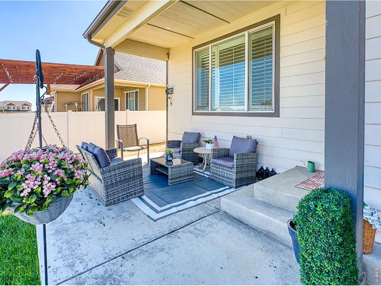 Covered patio with wicker seating, a hanging basket of pink flowers, and a white privacy fence.