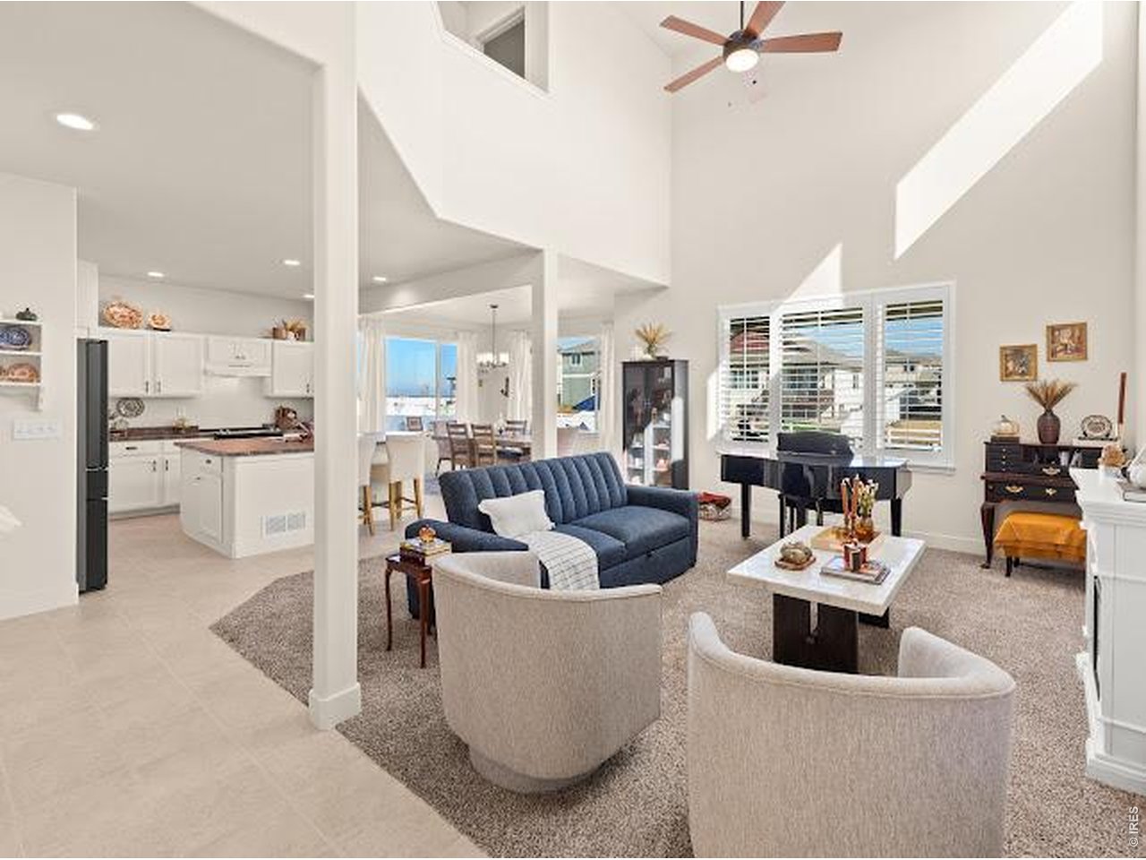 Open-plan living room with vaulted ceiling, blue sofa, and adjoining white kitchen.