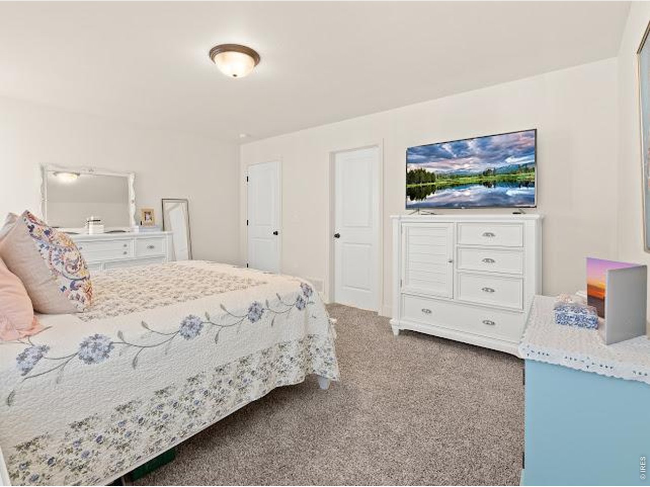 Bedroom with a floral bedspread, white dresser, and television.