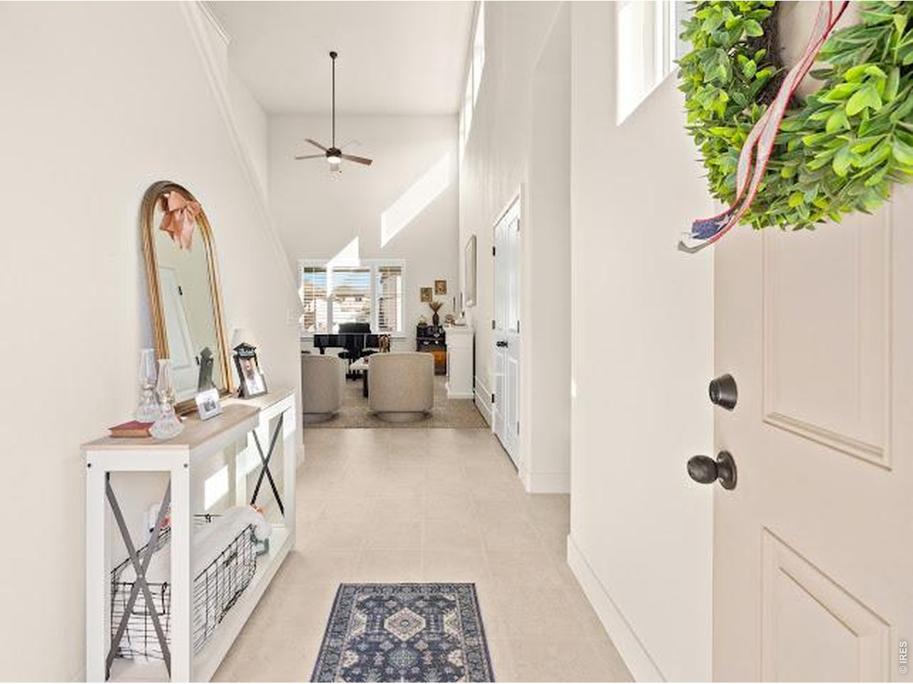 Bright entry hall with a patterned runner, arched mirror, and view into the living room.