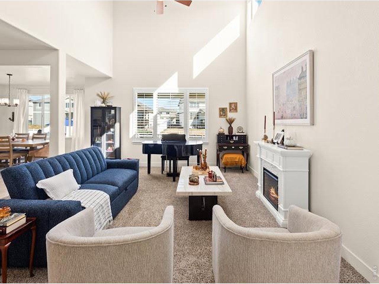 Living room with a vaulted ceiling, blue sofa, piano, and white fireplace.