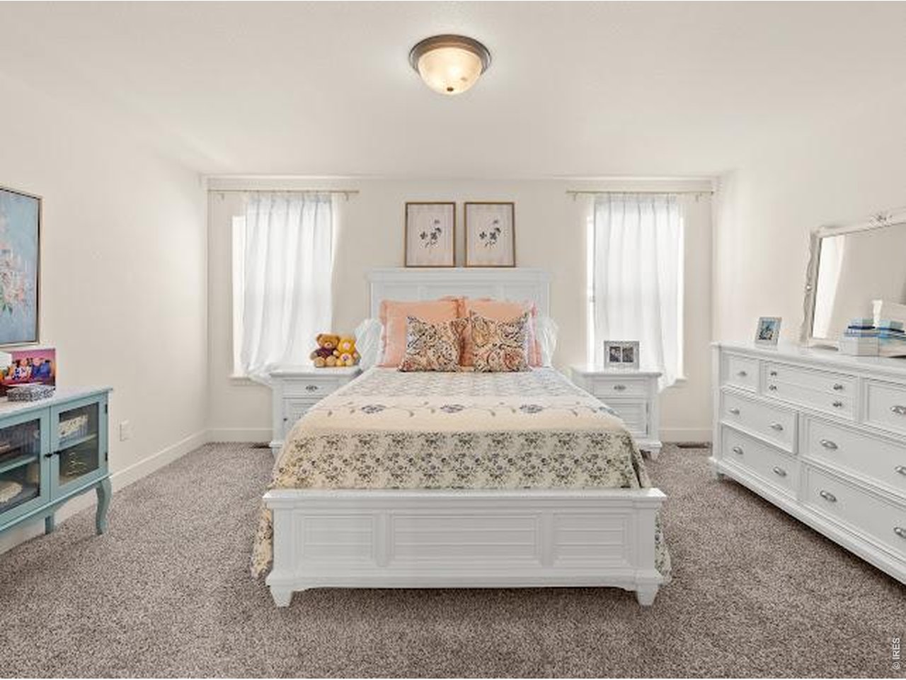 Bedroom with a white bed, matching bedside tables, two bright windows, and a white dresser.