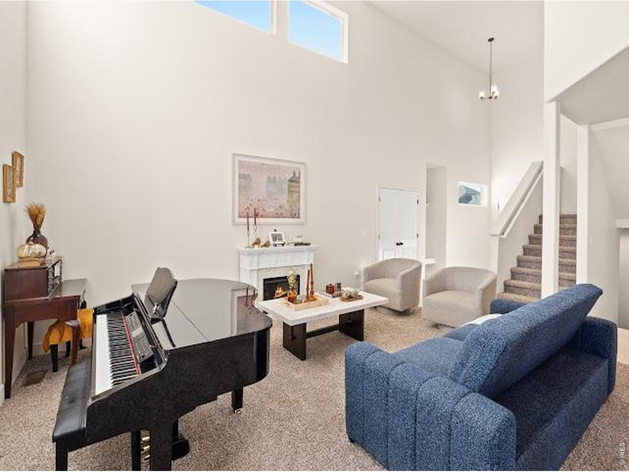 Living room with a grand piano, white fireplace, blue sofa, and staircase beneath a vaulted ceiling.