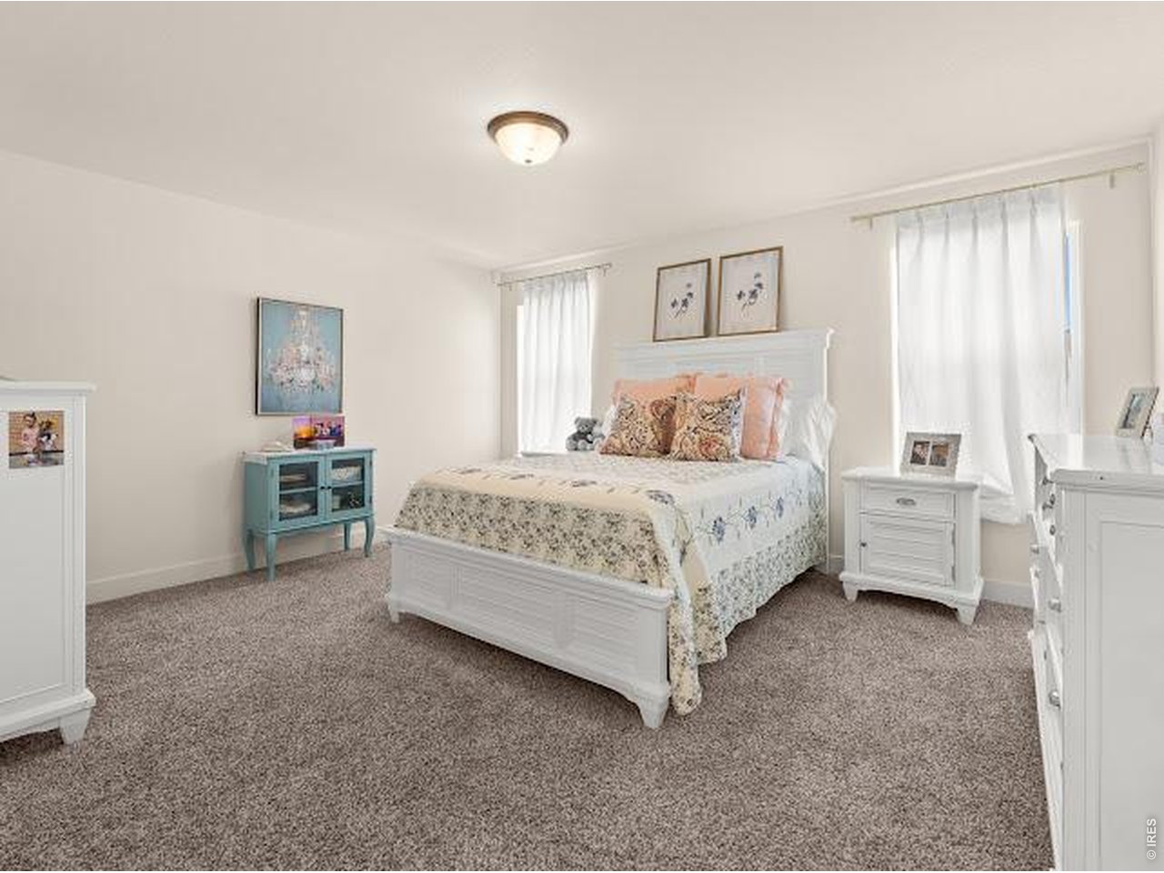 Staged bedroom with a white bed, patterned bedding, gray carpet, and turquoise cabinet.