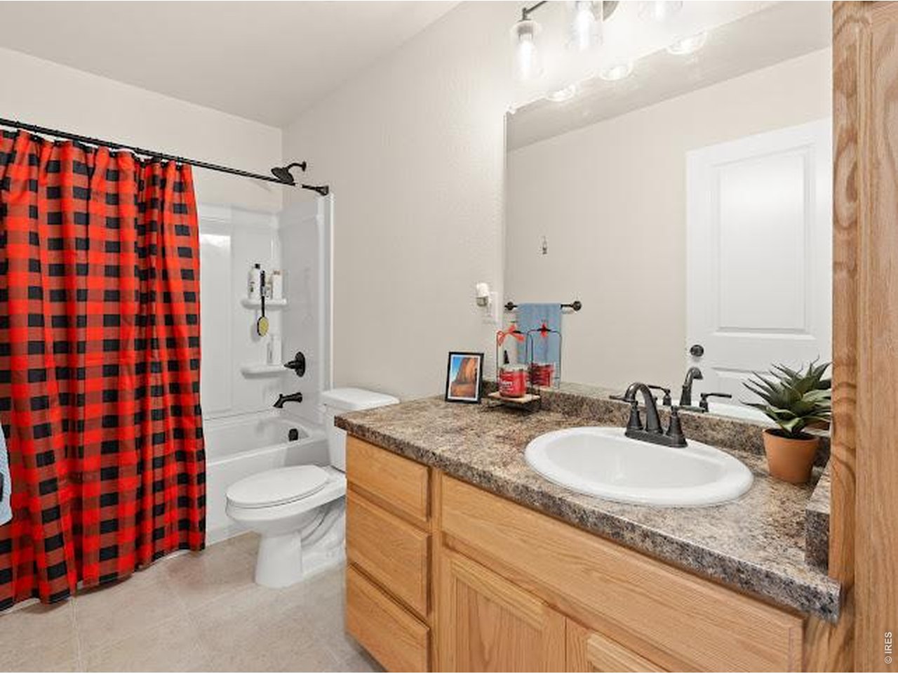 Bathroom with a plaid shower curtain and wood vanity topped by a speckled counter.