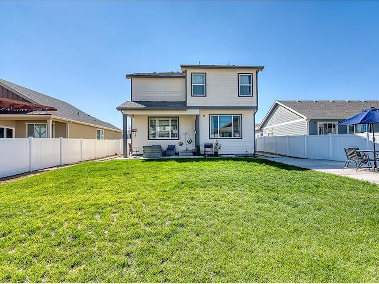 Two-story home behind a broad green lawn, with white fencing and patio seating.