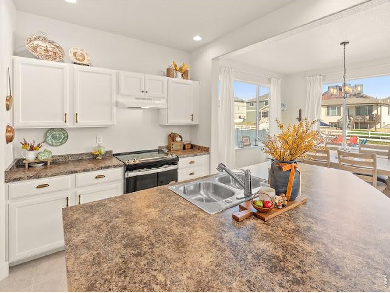 Staged kitchen with white cabinets, granite counters, and a large island sink beside bright dining-area windows.