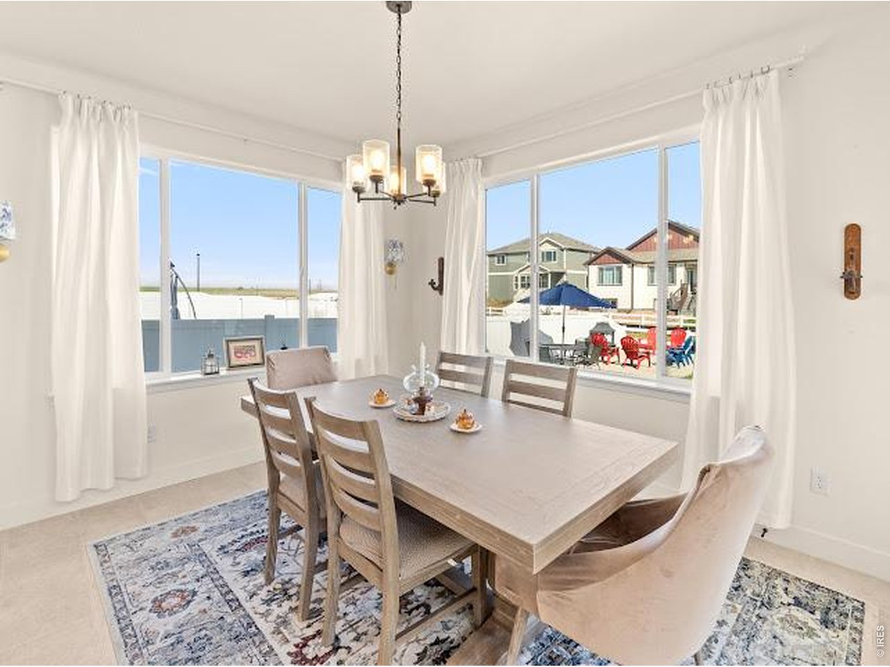 Dining room with a wood table and large windows overlooking a fenced patio.