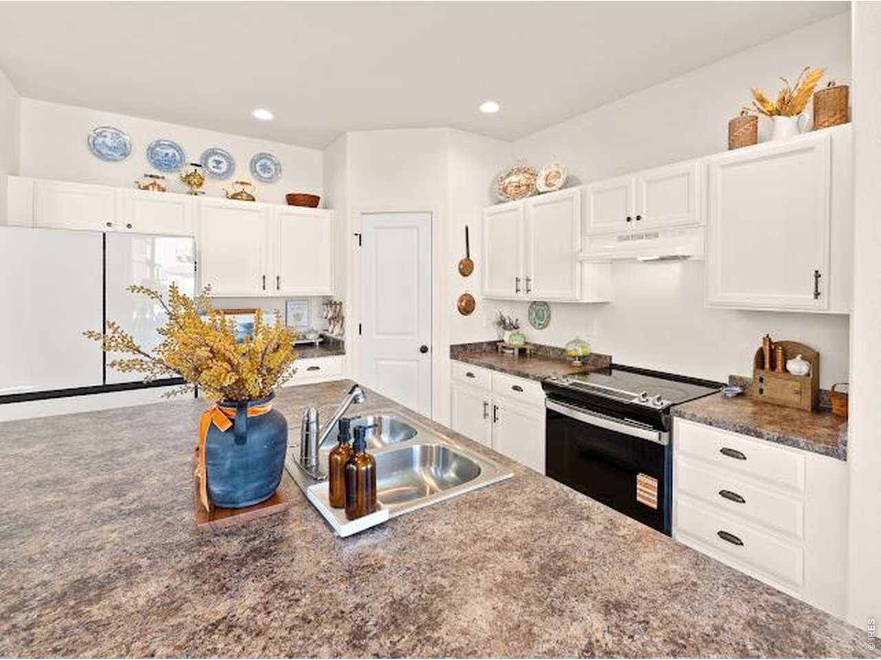 Bright kitchen with white cabinets, a large stone island, double sink, and black-and-stainless range.