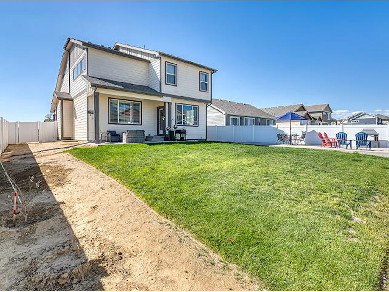 Two-story house with a fenced backyard, broad green lawn, and patio seating.