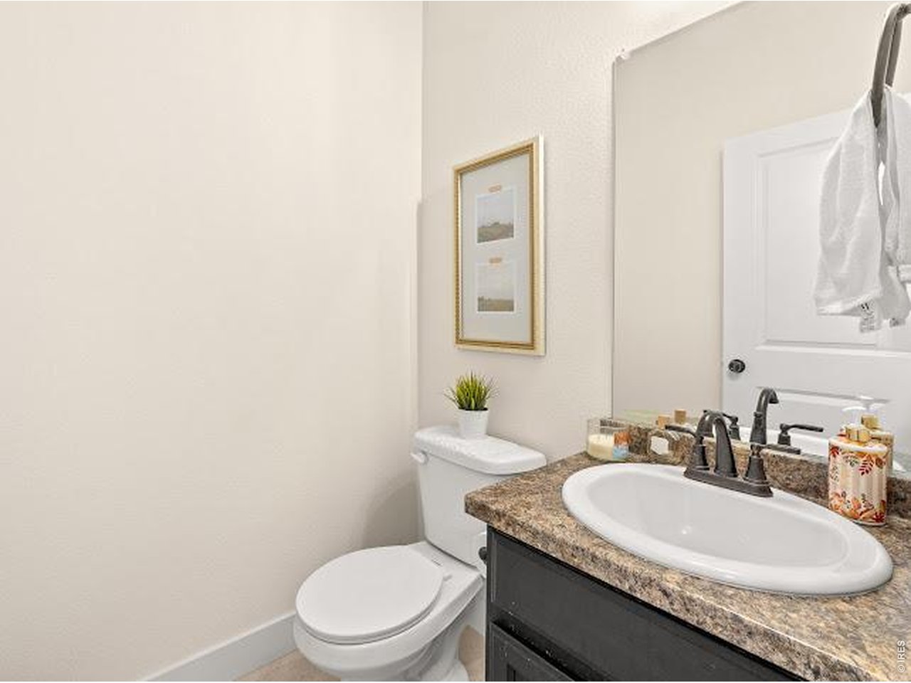 Bathroom with a granite countertop, oval sink, dark vanity, and white toilet.