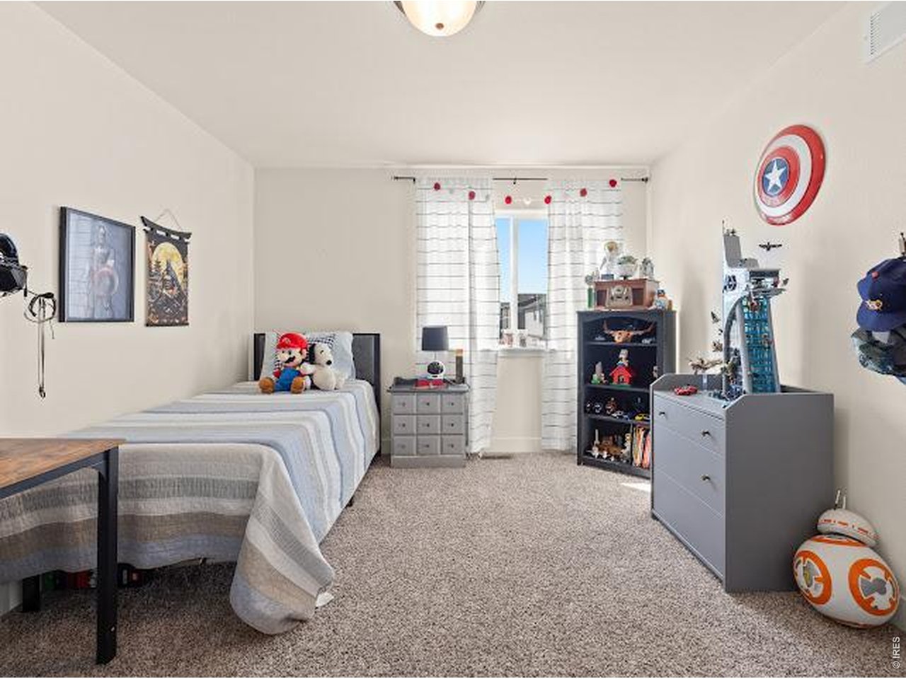 Bedroom with twin beds, beige carpet, and shelves of toys and superhero-themed decor.