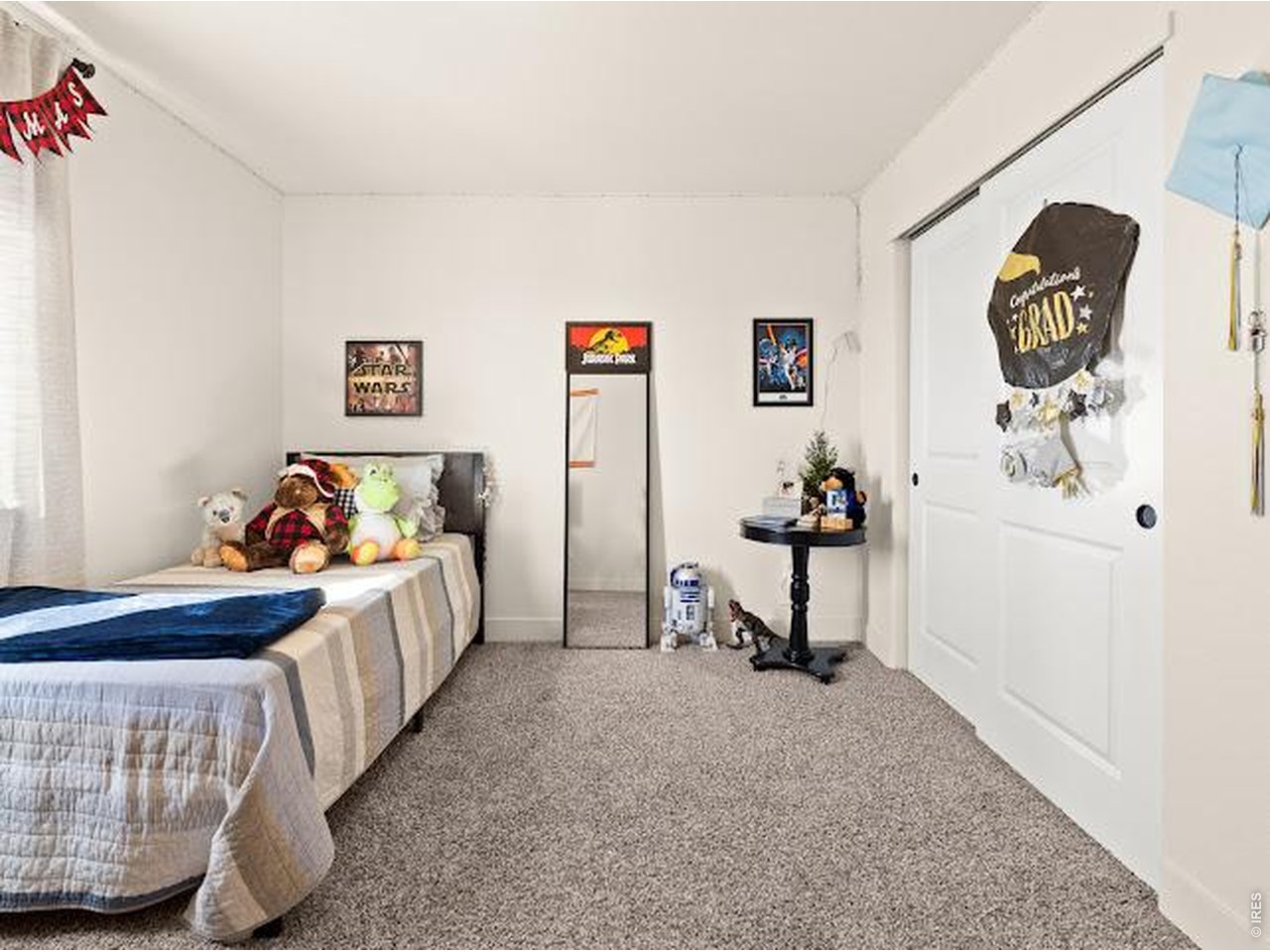 Bedroom with twin beds, plush toys, Star Wars decor, and a graduation decoration on the closet door.