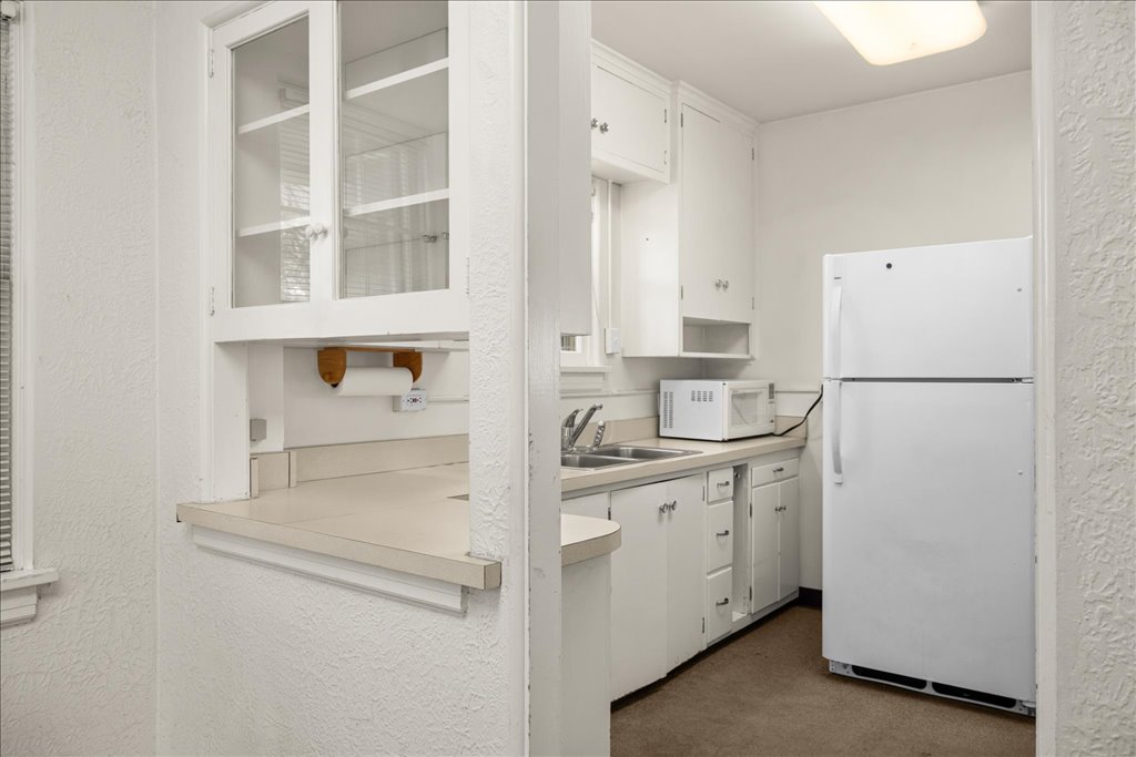 Compact white kitchen with a pass-through counter, double sink, microwave, and refrigerator.