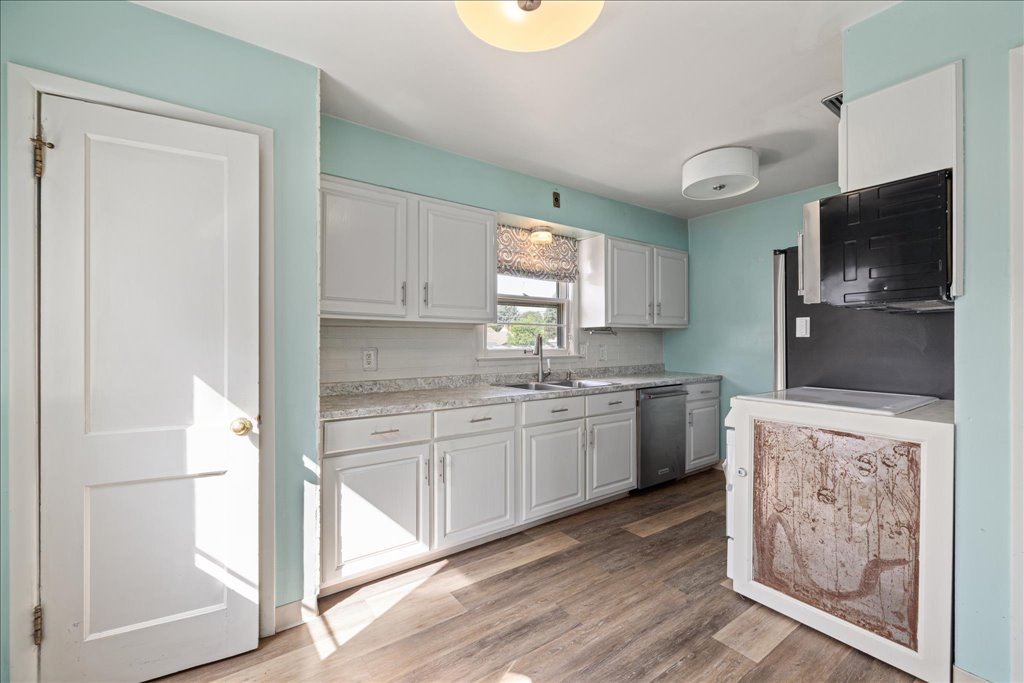 Kitchen with white cabinets, aqua walls, a window above the sink, and wood-look flooring.