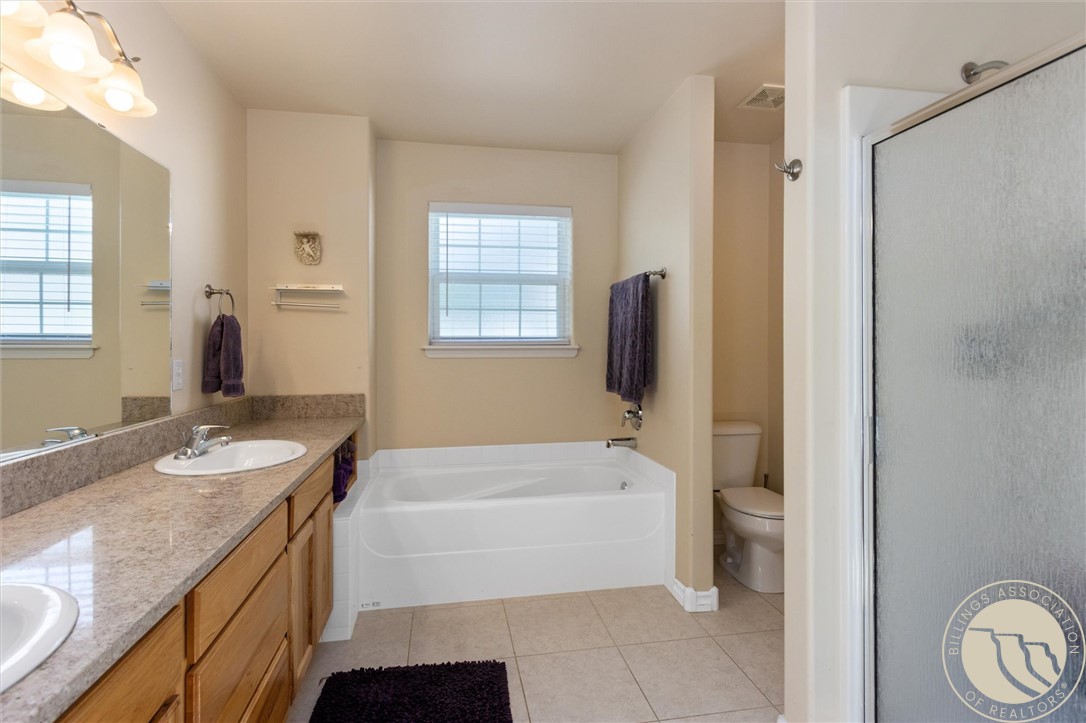 Bathroom with granite double-sink vanity, white bathtub, and separate toilet alcove.