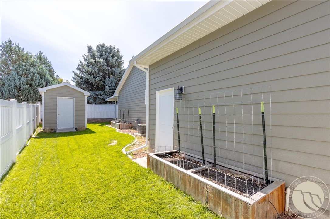 Backyard with raised garden beds, a small shed, green lawn, and white privacy fence.