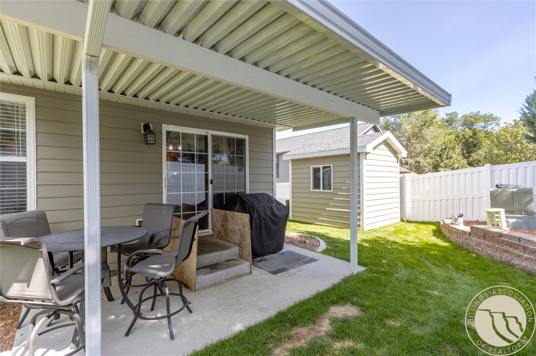 Covered backyard patio with outdoor dining furniture, a grill, detached shed, and fenced lawn.