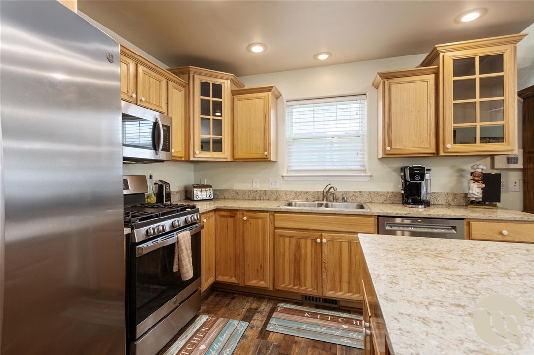 Kitchen with honey-toned wood cabinets, granite counters, stainless steel appliances, and a large peninsula.