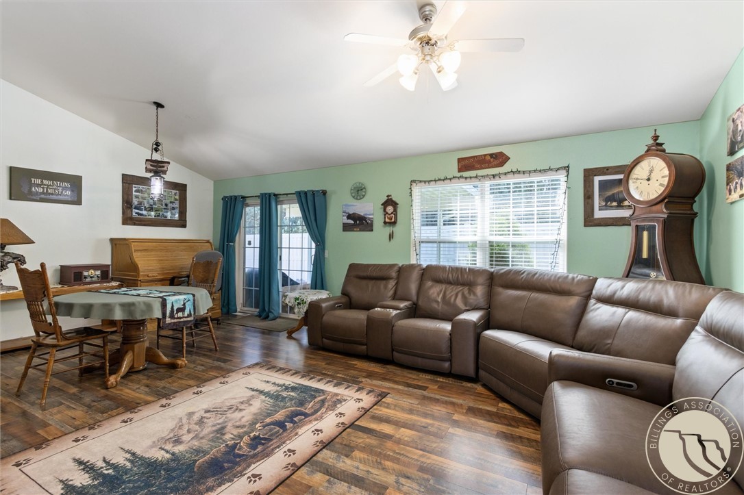 Living and dining room with a brown leather sectional, wildlife rug, and blue-curtained windows.
