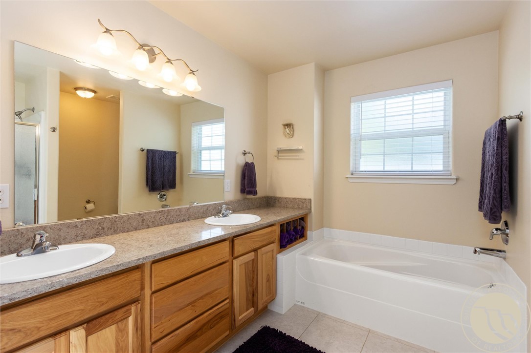 Bathroom with a double-sink wood vanity and a bathtub beneath a window.