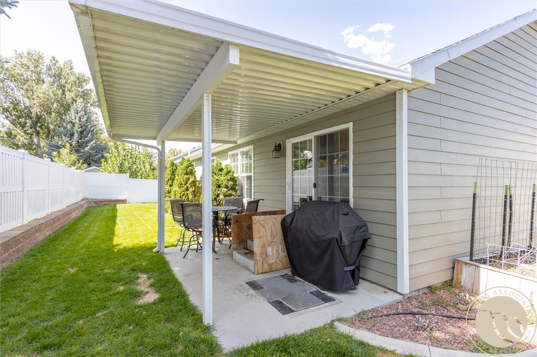 Covered backyard patio with outdoor dining set and grill beside a fenced lawn.