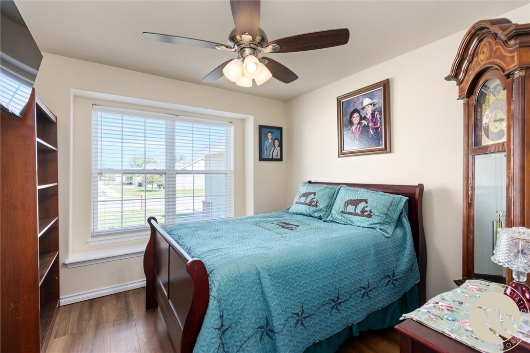 Bedroom with a turquoise quilted bed, large window, ceiling fan, and wooden grandfather clock.