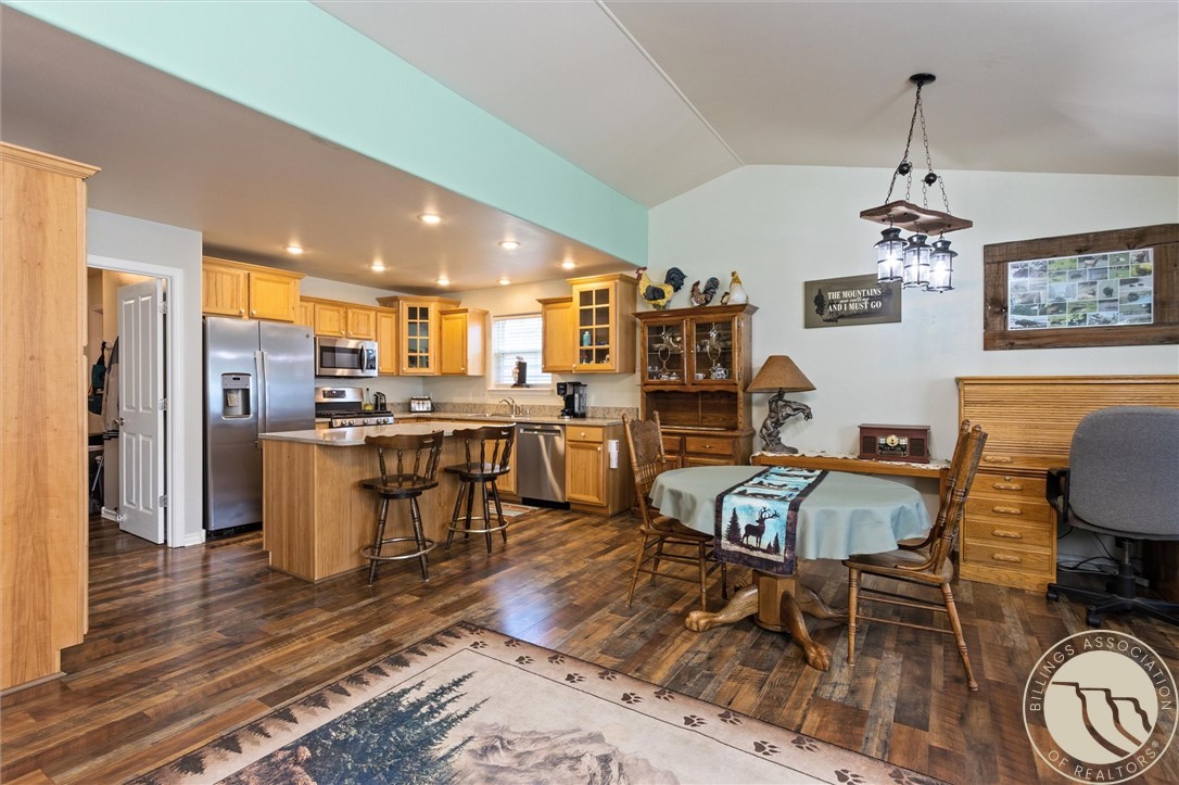 Open kitchen and dining area with wood cabinetry, breakfast island, stainless steel appliances, and vaulted ceiling.