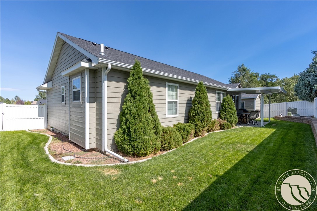 Gray-sided home with a fenced green backyard, landscaped shrubs, and a covered patio.