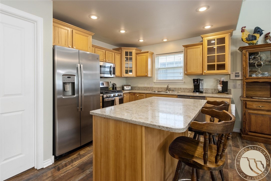 Kitchen with honey-colored cabinets, stainless steel appliances, and a large granite island with wooden stools.