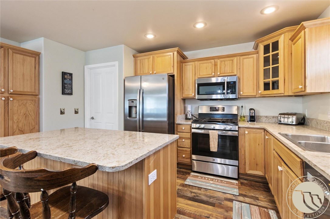Kitchen with a granite island, honey-toned cabinets, and stainless steel appliances.