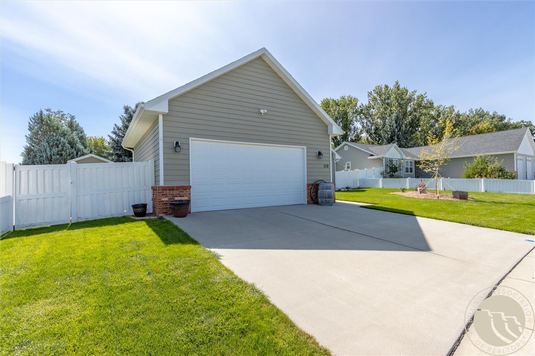 Gray detached garage with a white double door, wide concrete driveway, and white fencing.