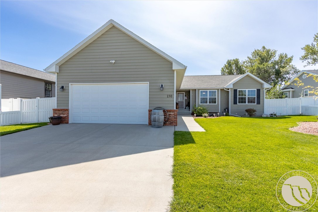 Gray single-story home with a large garage, broad driveway, green lawn, and white fence.