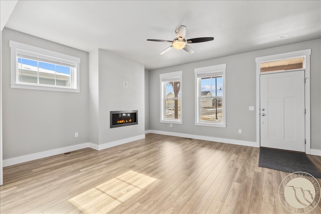 Empty living room with a modern fireplace, light wood floors, and large windows.
