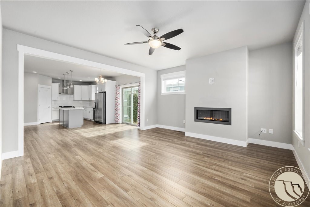 Open-plan living room and kitchen with wood-look floors, a linear fireplace, and white cabinetry.