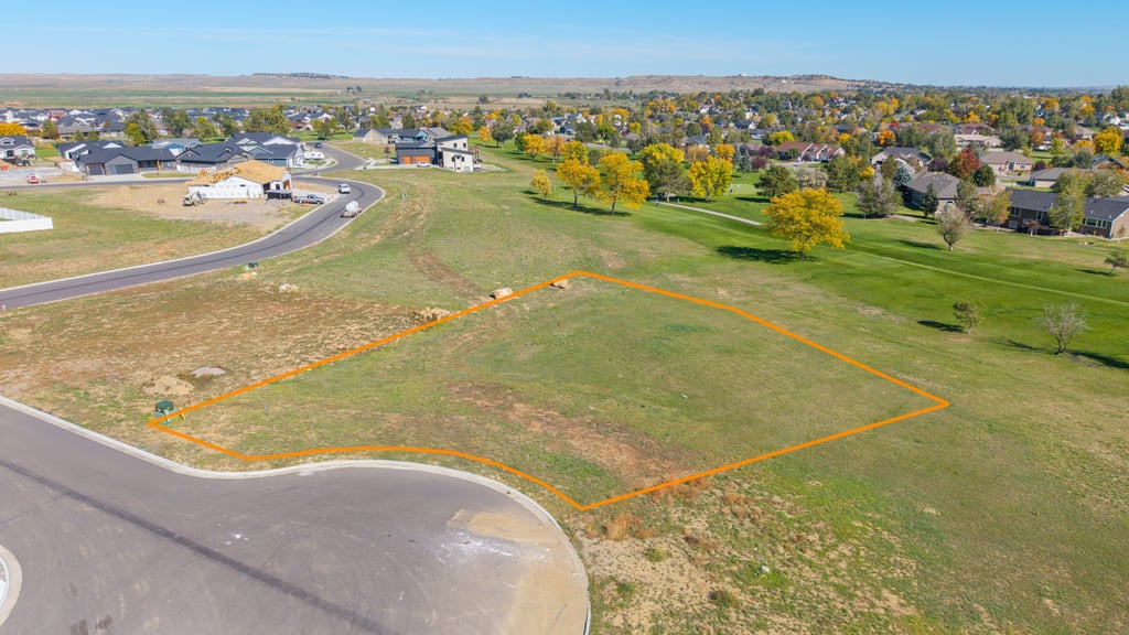 Vacant grassy lot outlined in orange beside a paved street in a residential neighborhood.