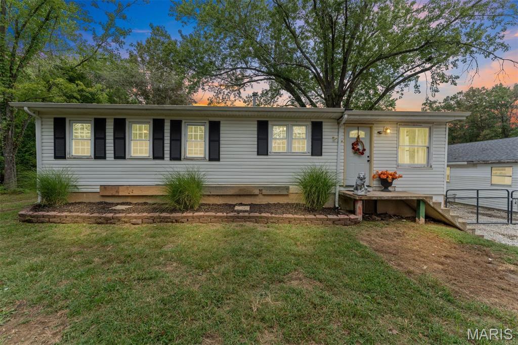 Single-story gray ranch house with black shutters, a raised entry porch, and a large tree overhead.